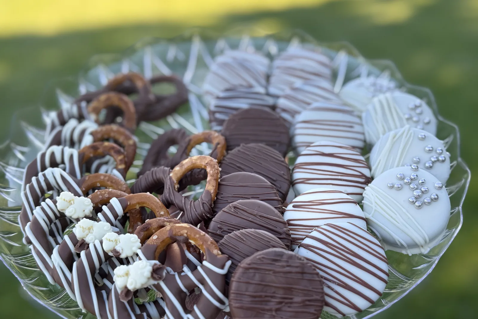 A platter of chocolate-dipped pretzels and Oreos with white drizzle, photographed in a garden